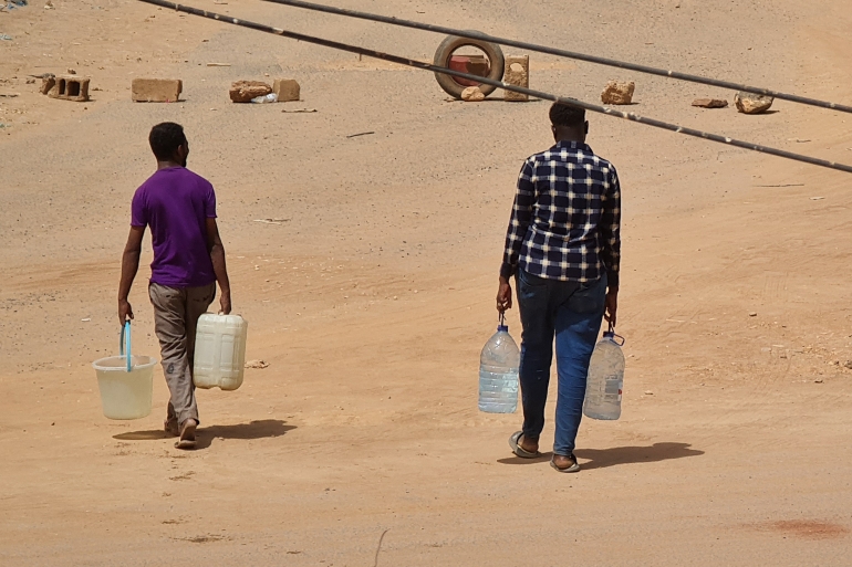 شابان يحملان دلوين من المياه في أحد أحياء الخرطوم