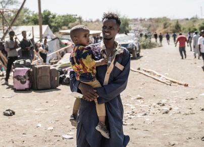 رجل يحمل طفلًا ونازحون سودانيون