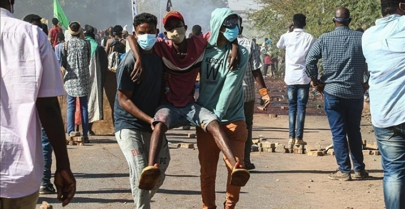 شابان يحملان متظاهرًا في أحد المواكب الرافضة للحكم العسكري بالخرطوم