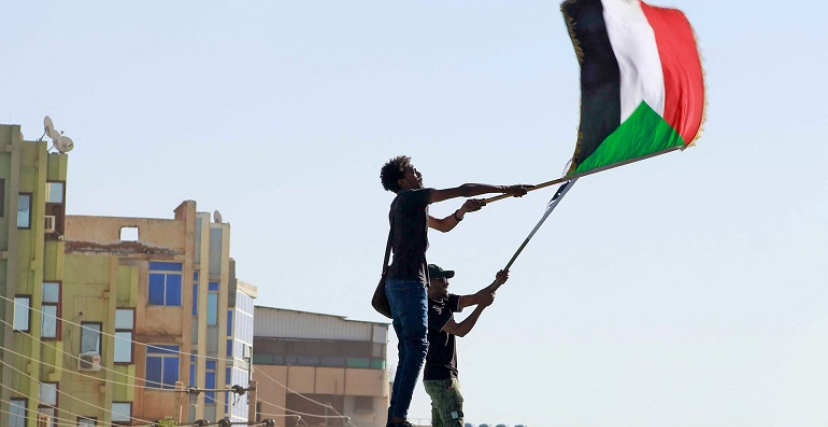 شاب يحمل علم السودان على رأس مبنى في إحدى التظاهرات