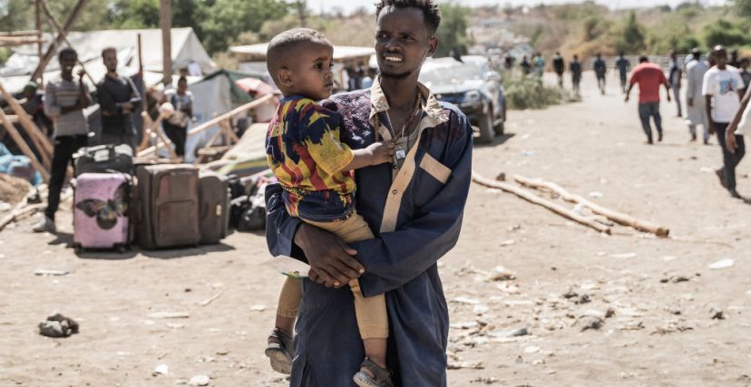 رجل يحمل طفلًا ونازحون سودانيون